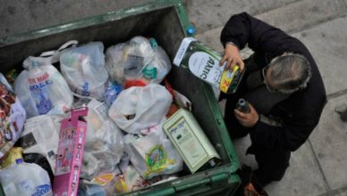 Een Griekse bedelaar verzamelt restjes uit blikken olijfolie in de vuilnisbakken om ze terug te verkopen