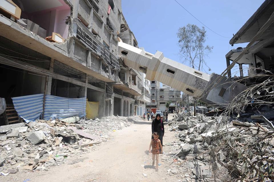 Een Palestijnse moeder en dochter stappen door wat ooit een winkelstraat en een minaret was in Gaza