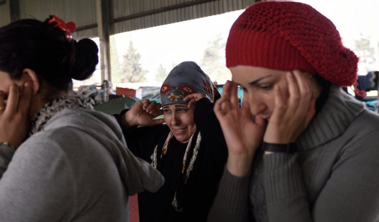Syrische vluchtelingen in Idomeni (aan de grens met Macedonië) stoppen hun oren af voor overvliegende jets van de Griekse luchtmacht. Deze geluiden kennen ze al.
